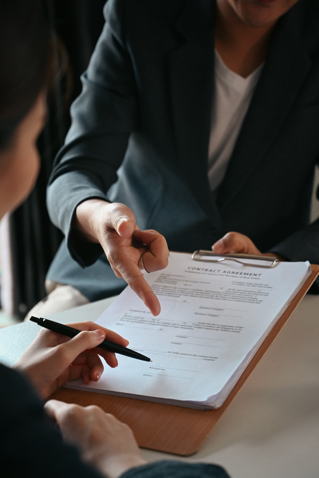 Cropped shot of businesswoman signing agreement with skilled lawyer on wooden table.